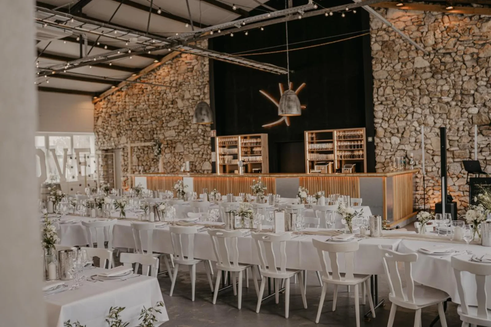Eventhalle des Kloster Kraul mit Natursteinwand, Bar und festlich gedeckten Hochzeitstafeln